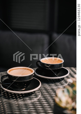 Two black coffee cups on a table in a cozy, modern cafe setting during the afternoon Two black coffee cups on a table in a cozy, modern cafe setting during the afternoon 128468130