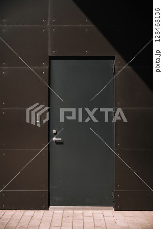 Modern dark door on a textured wall with geometric shadows in bright sunlight 128468136