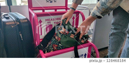 Person fitting bag into airport baggage sizer (pink frame). Carry-On Bag Airport Sizer Check - Travel Essentials, Hand Luggage, Budget Airline Rules 128468184