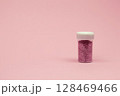 A glass jar brimming with fine pink shimmer is placed on a soft pink surface, glowing with light in a detailed close-up. 128469466