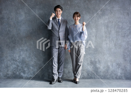 グレーの背景でスーツを着た男女のビジネスの全身 ガッツポーズ　カメラ目線	　 128470285