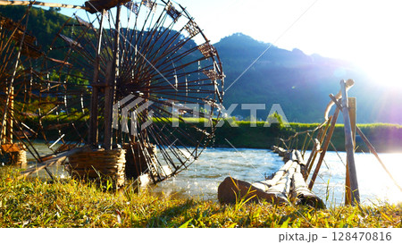 Wood water wheel Baler Machine in Agriculture Farm impeller lifted pumping water in river. Wooden Water Baler Machine green garden Farm blades by windy natural. Sustainable Resources Environment 128470816