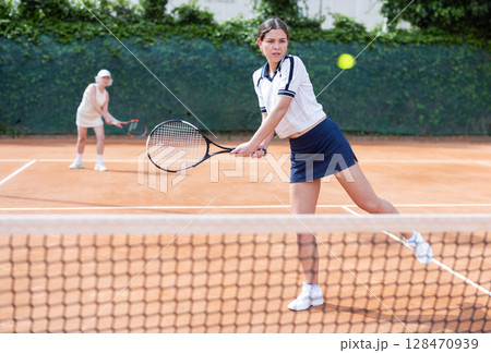 Middle aged and senior women plays tennis on open court with opponent. 128470939