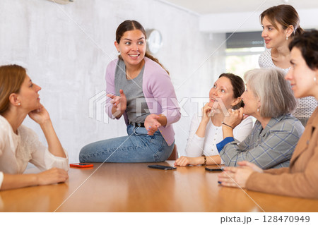 young girl student sits on table near friends and promotes version of solution of educational task young girl student sits on table near friends and promotes version of solution of educational task 128470949