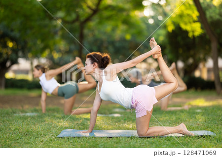 Happy sporty skilled young women going table pose of yoga with group in park at daytime Happy sporty skilled young women going table pose of yoga with group in park at daytime 128471069