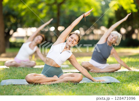 Girl stretching in lotus position at group yoga class outdoors Girl stretching in lotus position at group yoga class outdoors 128471096
