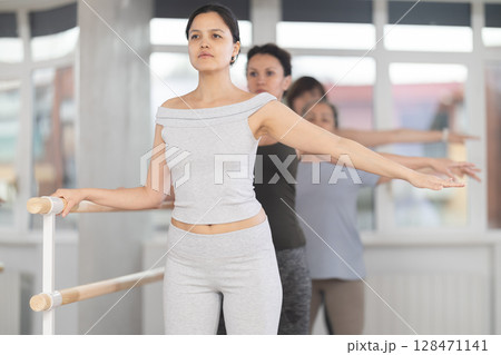 Women of different ages exercise near the ballet barre at group training session in batman batyu position Women of different ages exercise near the ballet barre at group training session in batman batyu position 128471141