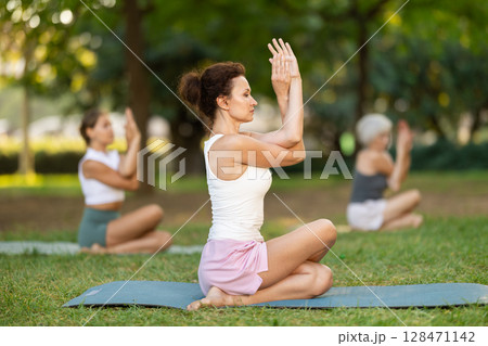 Woman performing Gomukhasana Garudasana outdoors with group Woman performing Gomukhasana Garudasana outdoors with group 128471142