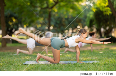 Girl performing balancing table asana during group yoga in park Girl performing balancing table asana during group yoga in park 128471146