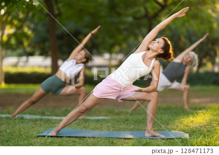 Woman performing Utthita Parsvakonasana at group yoga session in park 128471173