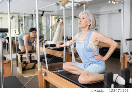 Senior woman doing stretching exercises on pilates reformer 128471191