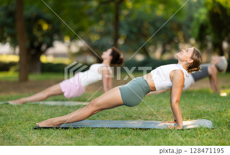 Girl doing Upward Plank Pose during group yoga in park 128471195
