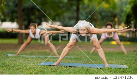 Young and mature women practicing different poses during group yoga training at park together 128471236