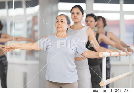 Women of different ages exercise near the ballet barre at group training session in batman batyu position 128471282