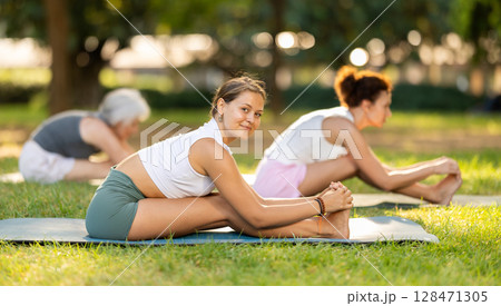 Girl enjoying yoga session on green glade with friends 128471305