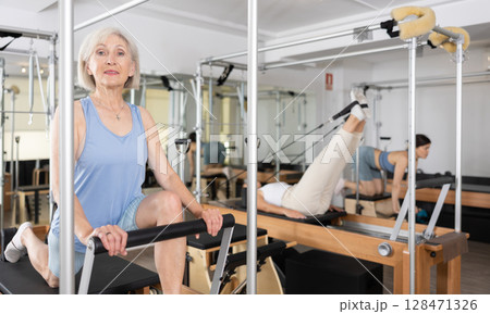 Senior woman doing stretching exercises on pilates reformer 128471326