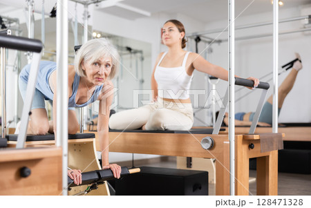 Elderly woman in sportswear training pilates performer bed in gym 128471328