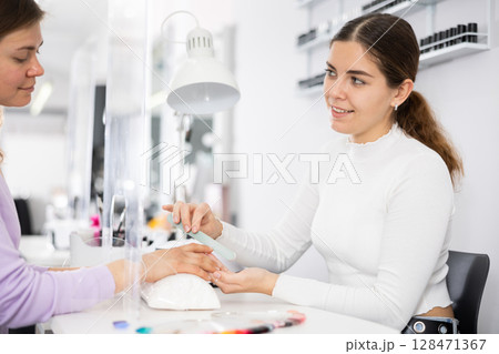 Friendly manicurist files the nails of a young female client Friendly manicurist files the nails of a young female client 128471367