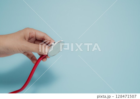 Hand Holding Red Stethoscope on Blue Background, Healthcare Concept Hand Holding Red Stethoscope on Blue Background, Healthcare Concept 128471507