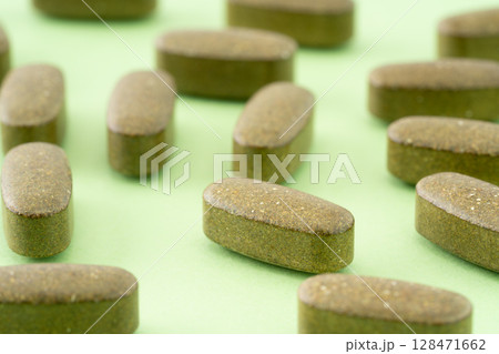 緑色の背景にカーキ色のサプリメントの錠剤(楕円形) 緑色の背景にカーキ色のサプリメントの錠剤(楕円形) 128471662