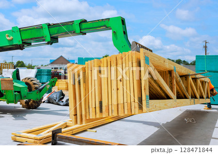 Construction worker uses green machine to lift wooden beams truss at site under works day time. Construction worker uses green machine to lift wooden beams truss at site under works day time. 128471844