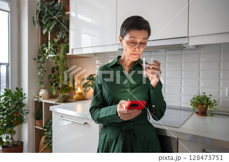 Focused female hydrating while engaged with phone content, trying to counteract stress effects Focused female hydrating while engaged with phone content, trying to counteract stress effects 128473751