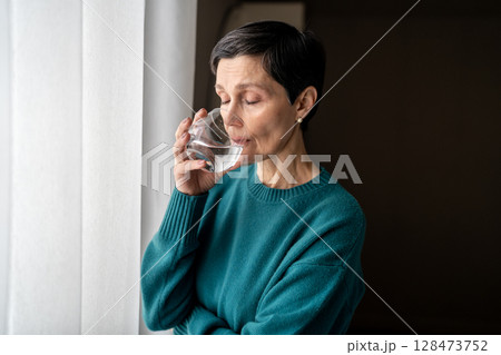 Sad calm woman sip water at window lost in thought isolated indoors. Nervous tension, self soothing Sad calm woman sip water at window lost in thought isolated indoors. Nervous tension, self soothing 128473752