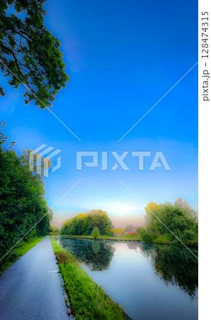 A serene and tranquil canal pathway surrounded by lush greenery and a clear blue sky above A serene and tranquil canal pathway surrounded by lush greenery and a clear blue sky above 128474315