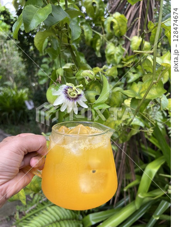 Hand holding a glass of passion fruit juice with passion fruit and passion flower in the garden 128474674