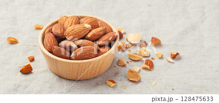 Almond nuts in wooden bowl with broken almonds on linen tablecloth background 128475633