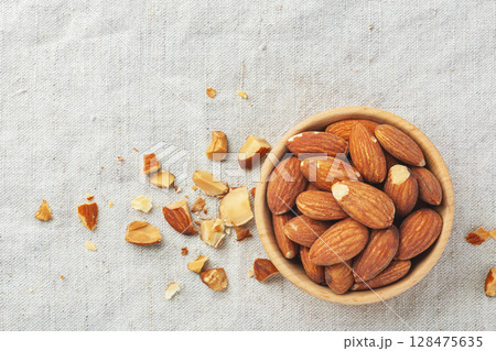 Roasted almonds in wood bowl  with broken almond on linen tablecloth background, top view 128475635
