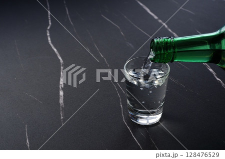 韓国の伝統的な蒸留酒、よく冷えた韓国焼酎(ソジュ)をグラスに注ぐ 韓国の伝統的な蒸留酒、よく冷えた韓国焼酎(ソジュ)をグラスに注ぐ 128476529