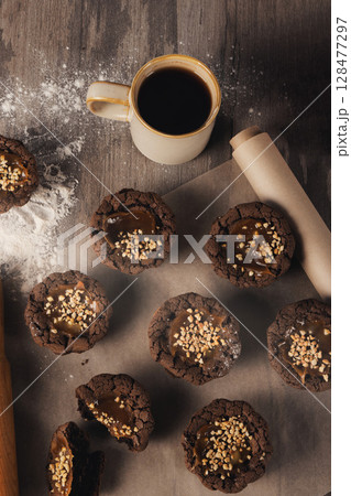 Freshly baked brown muffins on baking paper, coffee mug, flour on a table, top view, vertical image. Freshly baked brown muffins on baking paper, coffee mug, flour on a table, top view, vertical image. 128477297