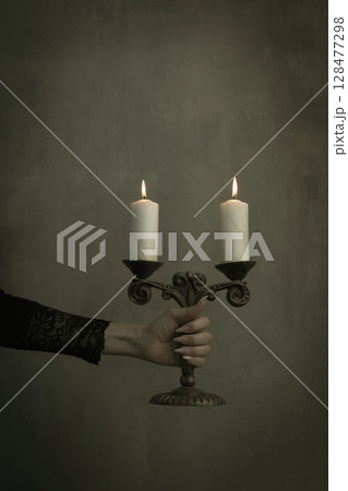 Female hand in black lace vintage sleeve hold old brass candelabrum with burning candles in the dark, vertical image. 128477298