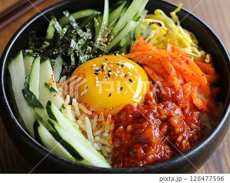Bibimbap, a Korean popular dish, typically consists of a bowl of warm rice topped with an assortment of ingredients such as vegetables, marinated meat, with spicy gochujang sauce. Bibimbap, a Korean popular dish, typically consists of a bowl of warm rice topped with an assortment of ingredients such as vegetables, marinated meat, with spicy gochujang sauce. 128477596
