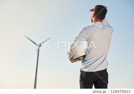 Rear view. Service engineer is on the field with windmills Rear view. Service engineer is on the field with windmills 128478023