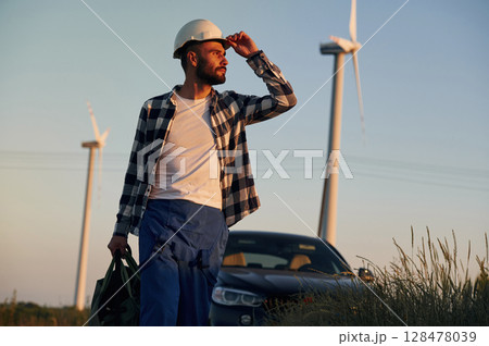 Walking with bag in hands, near car. Service engineer is on the field with windmills 128478039