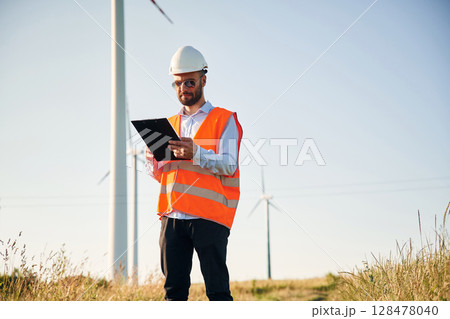 In orange colored uniform. Service engineer is on the field with windmills 128478040