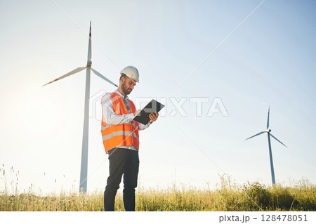 Black notepad in hands. Service engineer is on the field with windmills 128478051