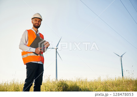 In orange colored uniform. Service engineer is on the field with windmills In orange colored uniform. Service engineer is on the field with windmills 128478053