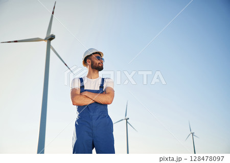 In blue colored uniform and in sunglasses. Service engineer is on the field with windmills 128478097