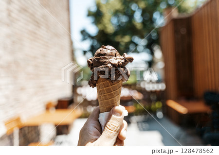 Chocolate Ice Cream Cone in Hand on a Summer Day 128478562