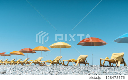 Colorful Beach Umbrellas and Sun Loungers on a Pebble Seaside 128478576