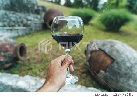 Glass of Red Wine with Traditional Georgian Qvevri in Rustic Setting 128478590