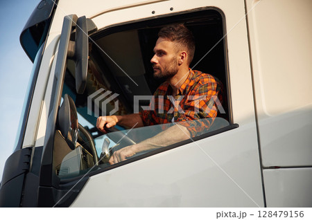 Looking through the door window, sitting inside. Young truck driver in casual clothes Looking through the door window, sitting inside. Young truck driver in casual clothes 128479156