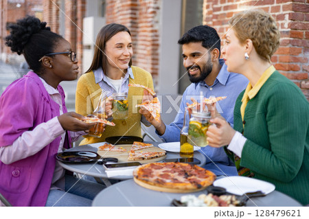 Diverse group of friends enjoying pizza and drinks outdoors, laughing and having a good time together. 128479621