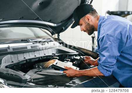Using tablet. Auto mechanic working in garage. Repair service 128479708