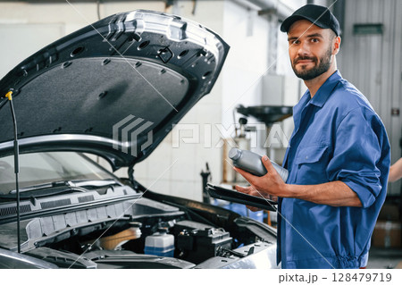 Grey colored oil can in hands. Auto mechanic working in garage. Repair service Grey colored oil can in hands. Auto mechanic working in garage. Repair service 128479719