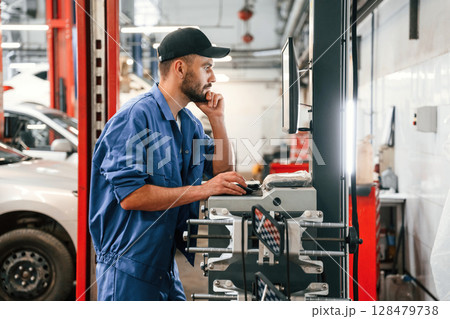 Standing by computer terminal. Auto mechanic working in garage. Repair service 128479738