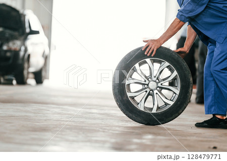 Walking with new tire. Auto mechanic working in garage. Repair service Walking with new tire. Auto mechanic working in garage. Repair service 128479771